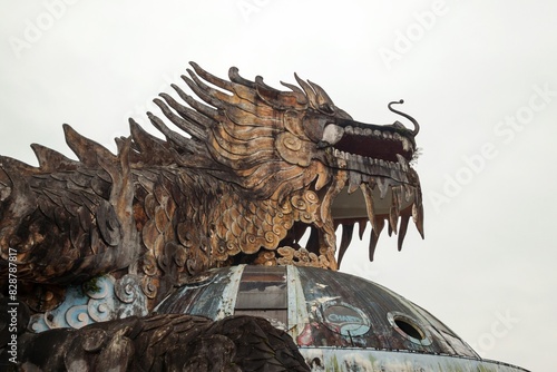 Intricately carved dragon head sculpture with fierce expression, bared teeth, vibrant paint, and flowing mane. Abandoned Waterpark in Hue, Vietnam.