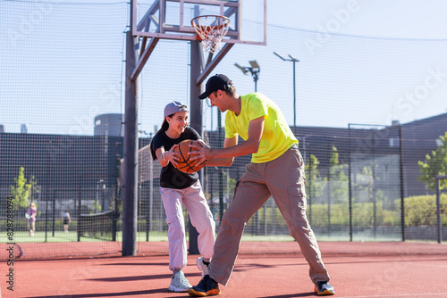 A happy father and teen daughter playing basketball outside at court. © Angelov