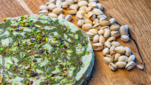 Pistachio cheesecake made from mascarpone and cream, with sprinkles, soruonded by pistachios nuts on a wooden table