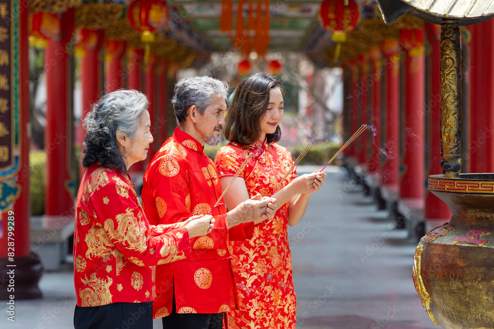 Obraz premium Asian family with senior parent in red cheongsam qipao dress is offering incense to the ancestral god inside Chinese Buddhist temple during lunar new year for best wish blessing and good luck