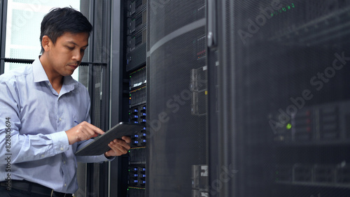 A technician in a blue shirt uses a tablet while inspecting a server rack in a modern data center, ensuring proper functionality.