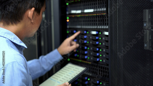 A technician in a blue shirt uses a tablet while inspecting a server rack in a modern data center, ensuring proper functionality.