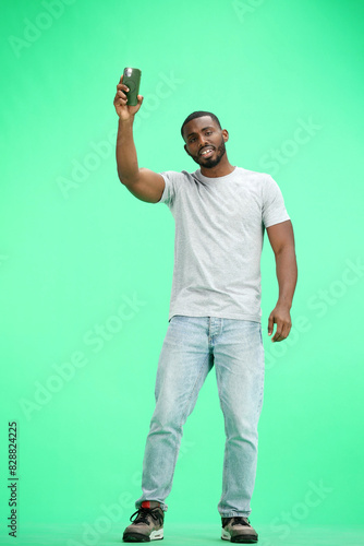 A man, full-length, on a green background, waving his phone