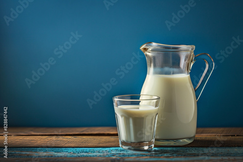 Milk in a glass and jug on a wooden table with a blue background