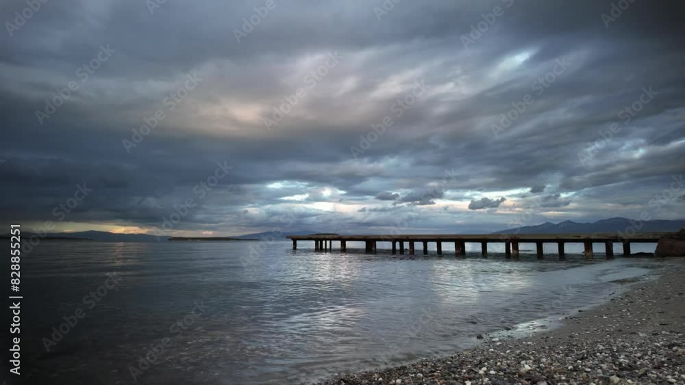 A pier on the coast, with a cloudy sky and water stretching to the horizon. The afterglow of dusk reflects off the wind waves on the natural landscape A pier on the coast, with a cloudy sky and water stretching to the horizon. The afterglow of dusk reflects off the wind waves on the natural landscape