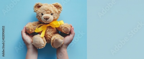 Photo of a person holding a teddy bear with a yellow ribbon around its lowered head, on a light blue background. Web banner with a wide angle view. photo