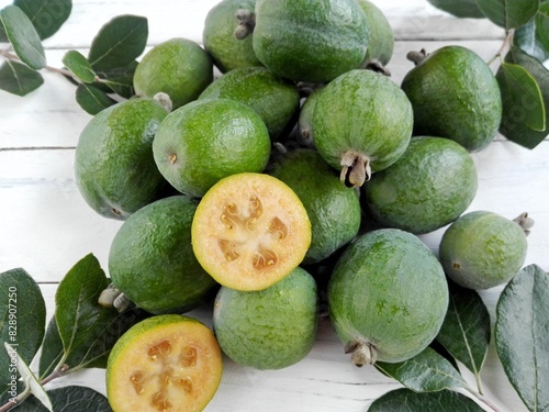 Green feijoa fruit cut & feijoa leaf (Acca sellowiana) pile on white wooden background. Tropical feijoa or pineapple guava fruit exotic green fruit. Raw acca sellowiana plant, guavasteen green fruit