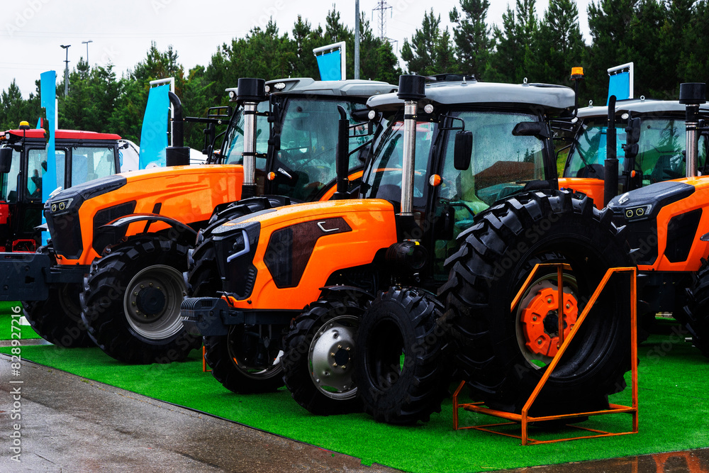 The new red agricultural tractors of various models stand in a row at the exhibition site in readiness for the start of spring sowing of agricultural The new red agricultural tractors of various models stand in a row at the exhibition site in readiness for the start of spring sowing of agricultural