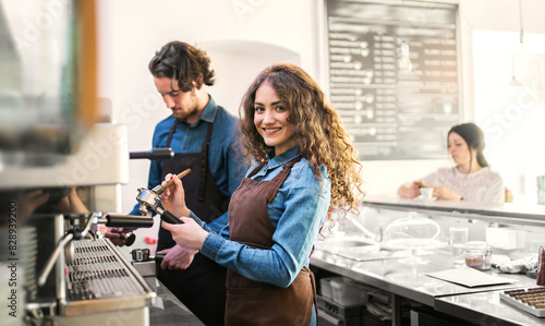 Two young baristas working in coffee shop, standing by counter. University students working part-time in cafe.