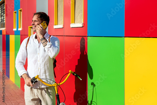 Man talking on phone leaning on bike against colorful wall photo