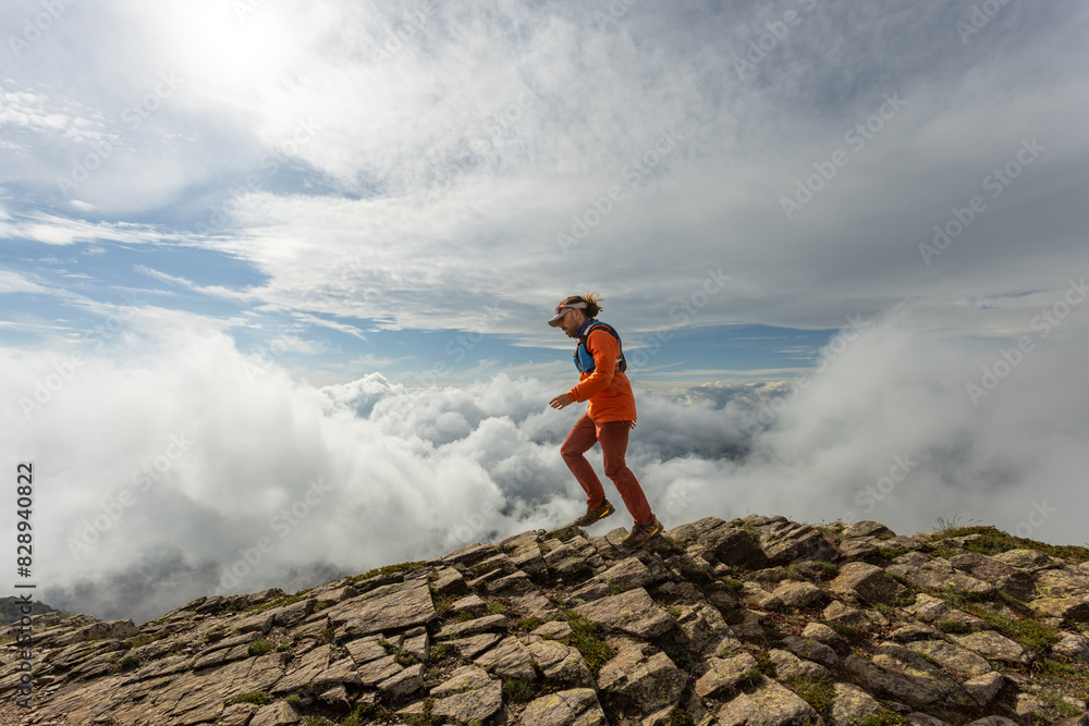 A person in an orange jacket is walking on a rocky mountain