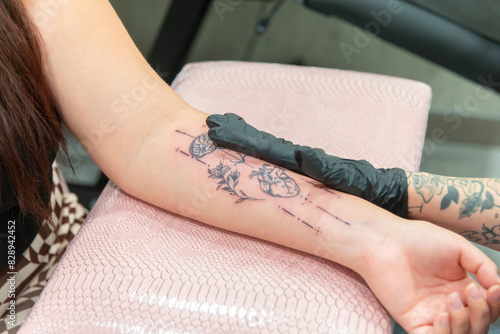 Anonymous artist creating a floral forearm tattoo photo