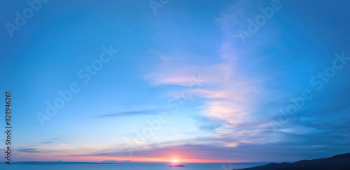 Photography Evening sky with pink clouds over a calm sea and distant mountains, creating a serene and tranquil scene at dusk