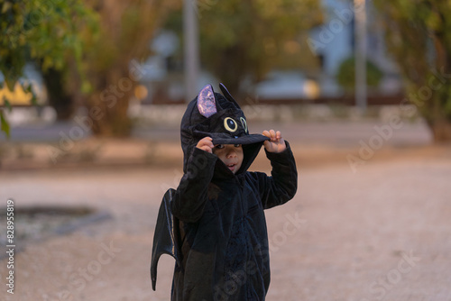 Принти на полотні A toddler dressed in a black bat costume plays peekaboo by lifting the hood over his eyes in a park during Halloween, adding to the festive and playful atmosphere