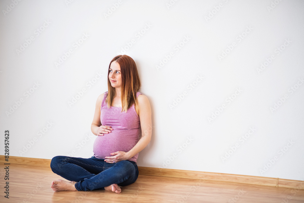Pregnant woman sitting on floor touching her belly.