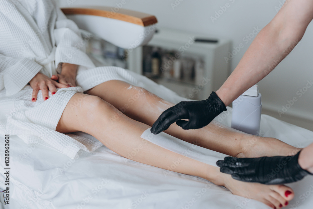 Fototapeta premium Beautician depilating young woman's legs with liquid sugar in spa center