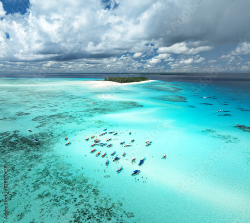 Aerial view of colorful boats in clear azure water in summer. Mnemba island, Zanzibar. Top drone view of sandbank in low tide, blue sea, white sand, swimming people, yachts, sky with clouds. Ocean