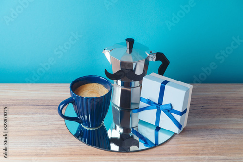 Happy Father's day concept with coffee maker, coffee cup, gift box and mirrored tray on wooden table over blue background