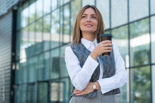Business woman standing outdoors and holding cup of coffee