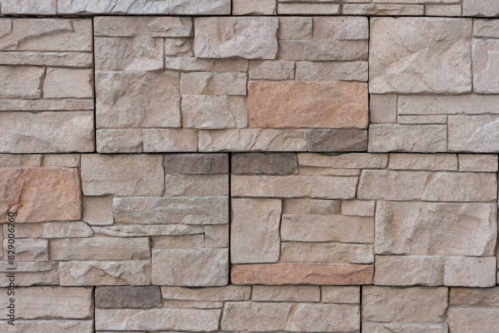 Fototapeta premium Close-up view of textured beige building wall surface covered with stone shaped tiles. Abstract construction industry background. Copy space. Soft focus. Decor materials theme.
