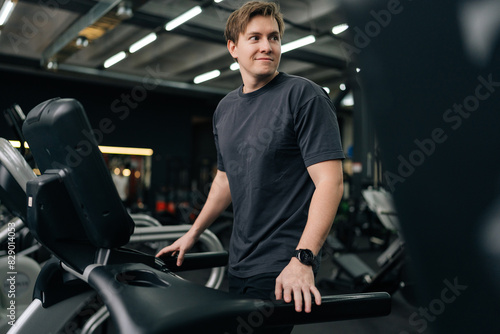 Smiling young man in sportswear walking on treadmill preforming warming-up run routine exercise in gym. Sporty male walking on running track, working on health and fitness. Concept of healthy life.