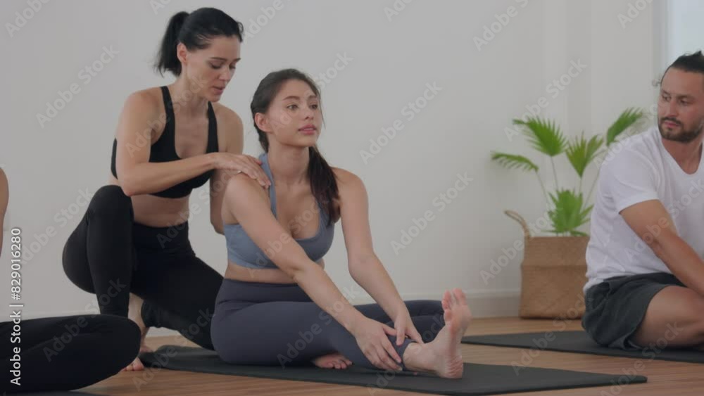 Group Yoga Class in a Bright Studio with Instructor Assisting in Seated Forward Bend Group Yoga Class in a Bright Studio with Instructor Assisting in Seated Forward Bend
