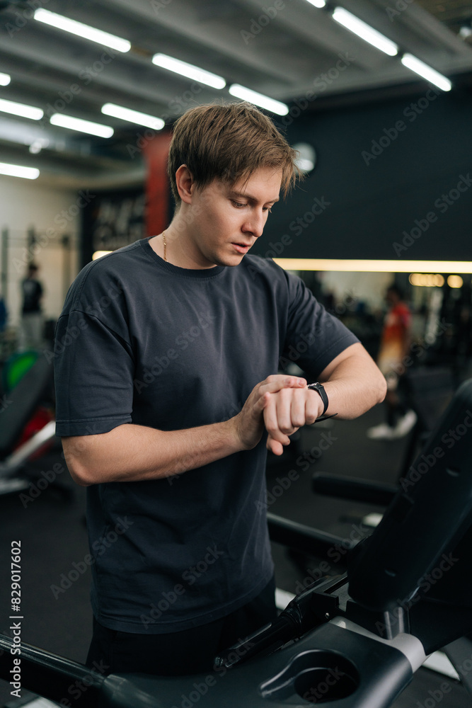 Vertical shot of handsome sportsman check health indicator and heart rate on smartwatch during workout strength training. Millennial athlete using fitness tracker during workout. Vertical shot of handsome sportsman check health indicator and heart rate on smartwatch during workout strength training. Millennial athlete using fitness tracker during workout.