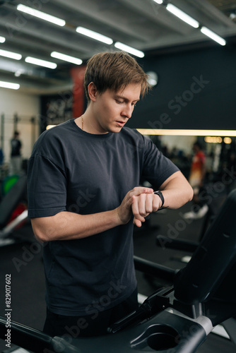 Vertical shot of handsome sportsman check health indicator and heart rate on smartwatch during workout strength training. Millennial athlete using fitness tracker during workout.