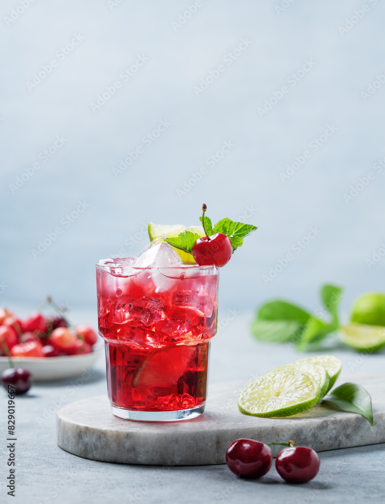 Cherry-lime mojito cocktail with mint, lime and ice on a marble board on a blue background.