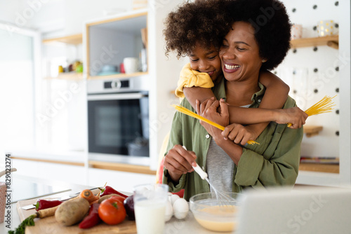 African American mother and daughter laughing and smiling while making pasta and playing with spaghetti straps in the kitchen.