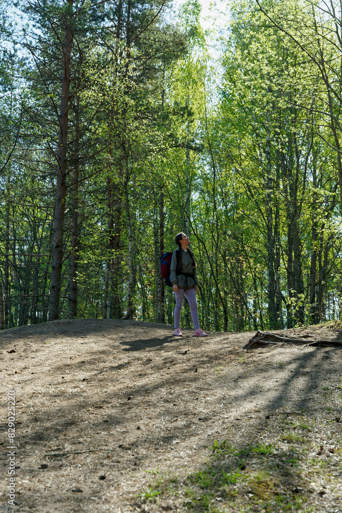 Woman stopped on a hill and looking up on trees while doing hike in spring forest Woman stopped on a hill and looking up on trees while doing hike in spring forest
