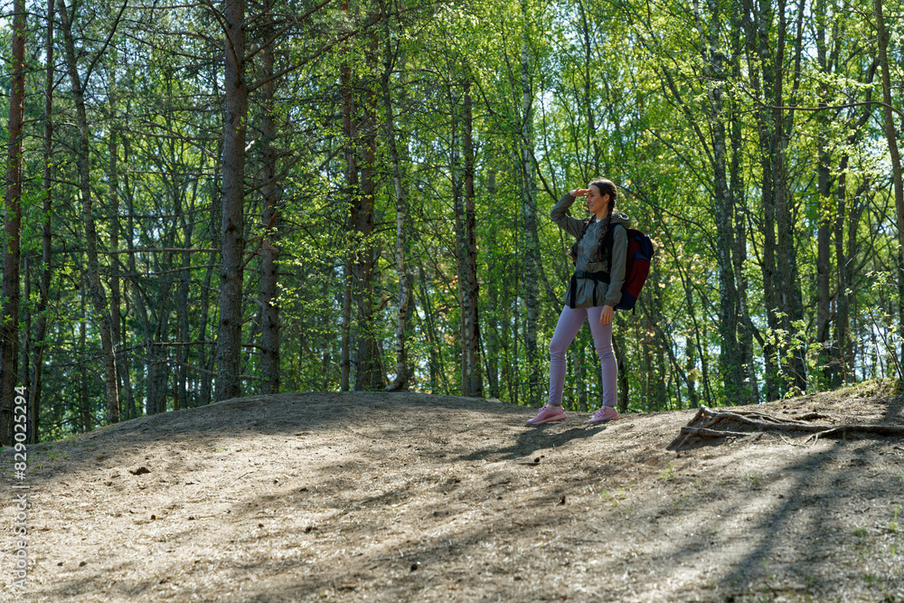 Young woman on hiking trail looking to landscape from small hill with one hand covering her face from sunlight Young woman on hiking trail looking to landscape from small hill with one hand covering her face from sunlight