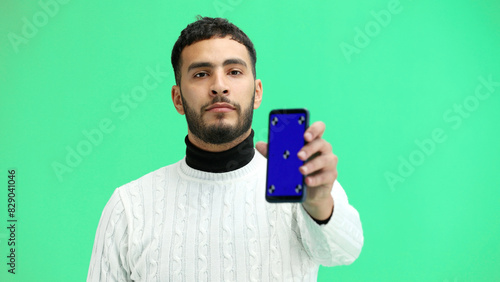 A man, close-up, on a green background, shows a phone © Katsiaryna