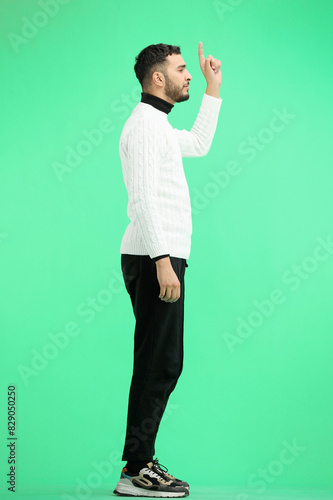 A man, full-length, on a green background, points up © Katsiaryna