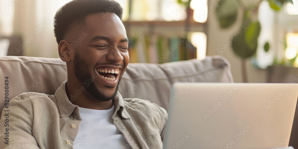 Joyous young man laughing at content on his laptop screen while sitting comfortably at home Joyous young man laughing at content on his laptop screen while sitting comfortably at home