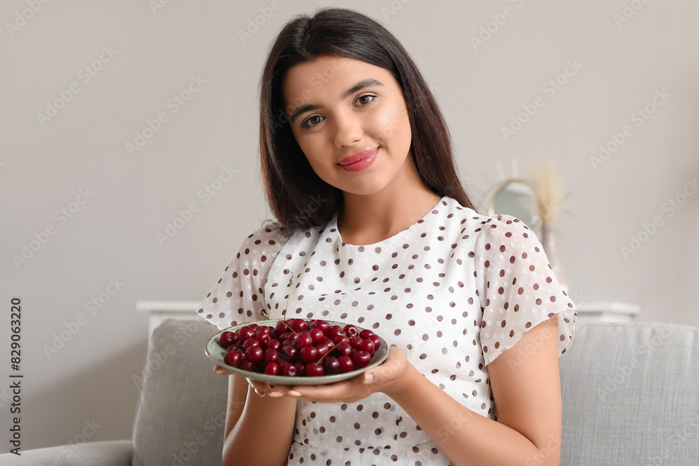 Happy beautiful young woman with bowl of ripe cherries sitting on sofa in living room Happy beautiful young woman with bowl of ripe cherries sitting on sofa in living room