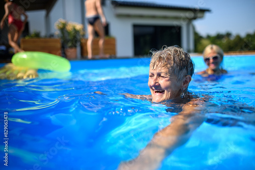 Group of cheerful seniors shaving fun in pool jumping  swiming and lounging on floats. Elderly friends spending hot day by swimming pool.