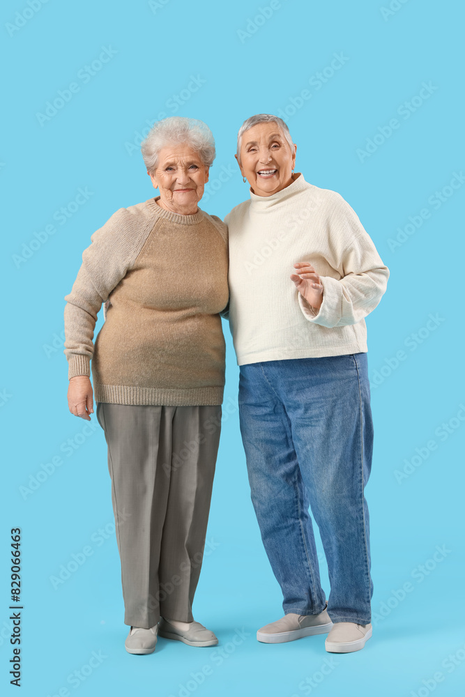 Senior female friends hugging on blue background Senior female friends hugging on blue background