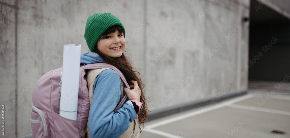 Outdoor portrait of cute young girl with beanie hat and backpack. Girl with long hair going to school. Banner with copy space.
