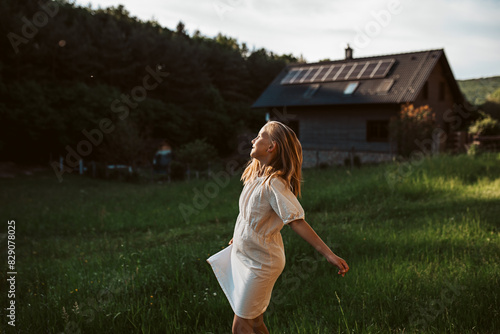 Little girl in front of house with solar panels on roof, jumping, dancing and having fun. Concept of renewable resources.