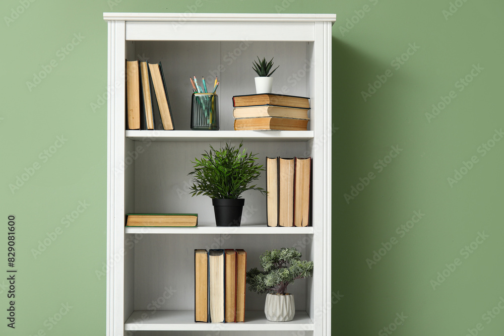 Bookcase with books and houseplants near green wall in room, closeup Bookcase with books and houseplants near green wall in room, closeup