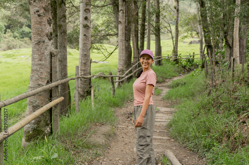 retrato de una mujer joven con ropa cómoda y gorra mientras sonríe al aire libre en medio de un camino forestal photo