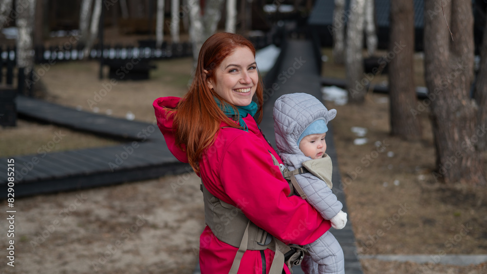 Obraz premium A Caucasian woman walks with her son in an ergo backpack in the countryside. 