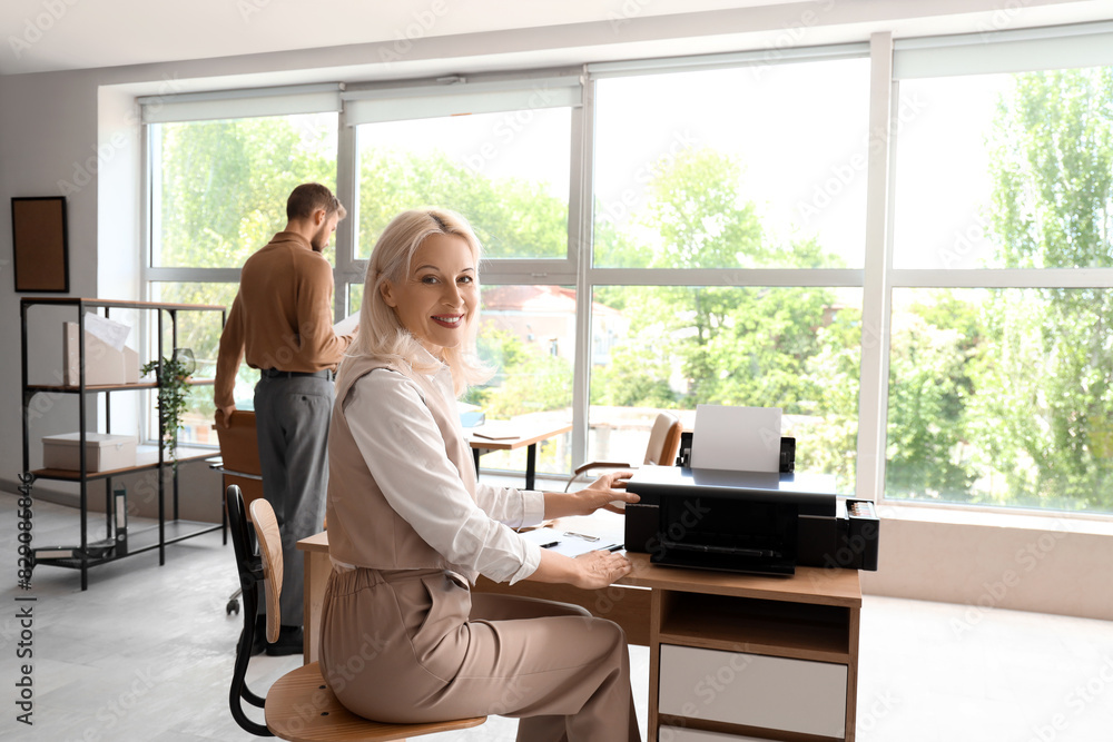 Mature businesswoman using printer at table in office Mature businesswoman using printer at table in office