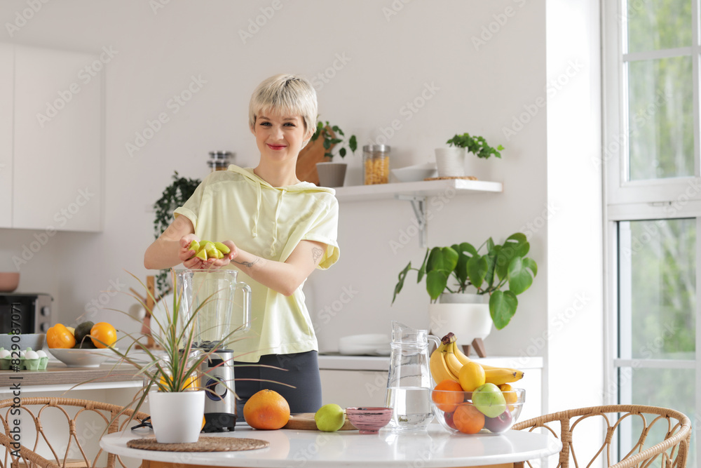 Sporty young woman putting cut apple into blender in kitchen