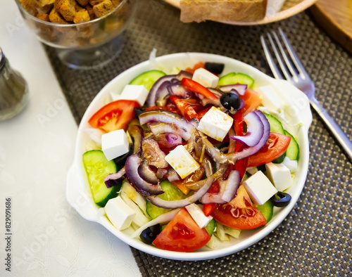 Fresh colorful Greek salad (horiatiki salad) served with feta cheese on white plate.