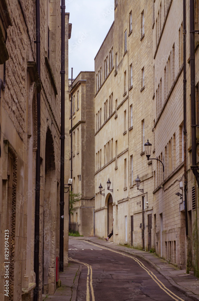 A narrow street flanked by tall stone buildings in the historic City of Bath in Somerset England A narrow street flanked by tall stone buildings in the historic City of Bath in Somerset England