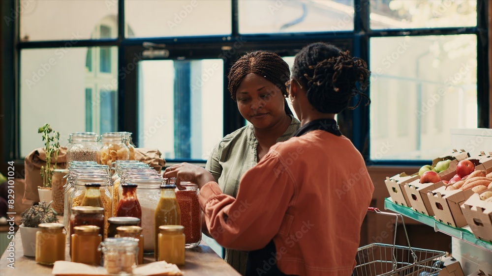 Vendor giving food sample to client to ensure natural sweetness, recommending the best organic products to frequent customer at local grocery store. Women supporting sustainable lifestyle concept. Vendor giving food sample to client to ensure natural sweetness, recommending the best organic products to frequent customer at local grocery store. Women supporting sustainable lifestyle concept.