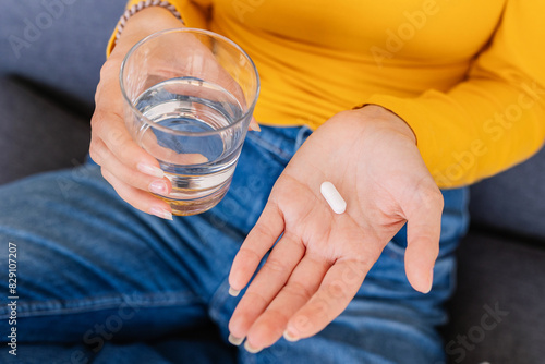 Close up young woman hands holding white pill and glass of water. Vitamins, pills and tablets. Health care and people concept. photo