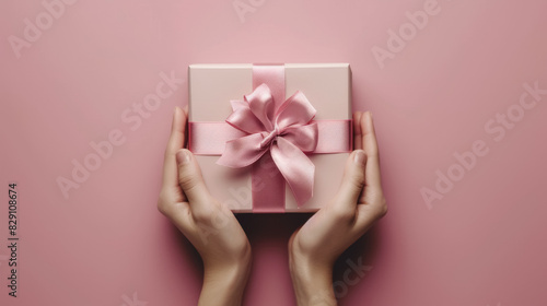 Hands holding pink gift box with ribbon on pink background © LabirintStudio